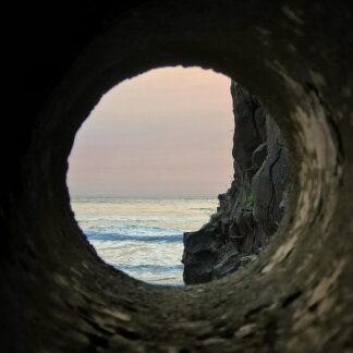 Cover of the Ruminant "Domicile Unknown" LP with a view of the ocean and sky at sunset. This is seen through the opening of a circular rock tunnel, where rugged rock formations frame the entrance.